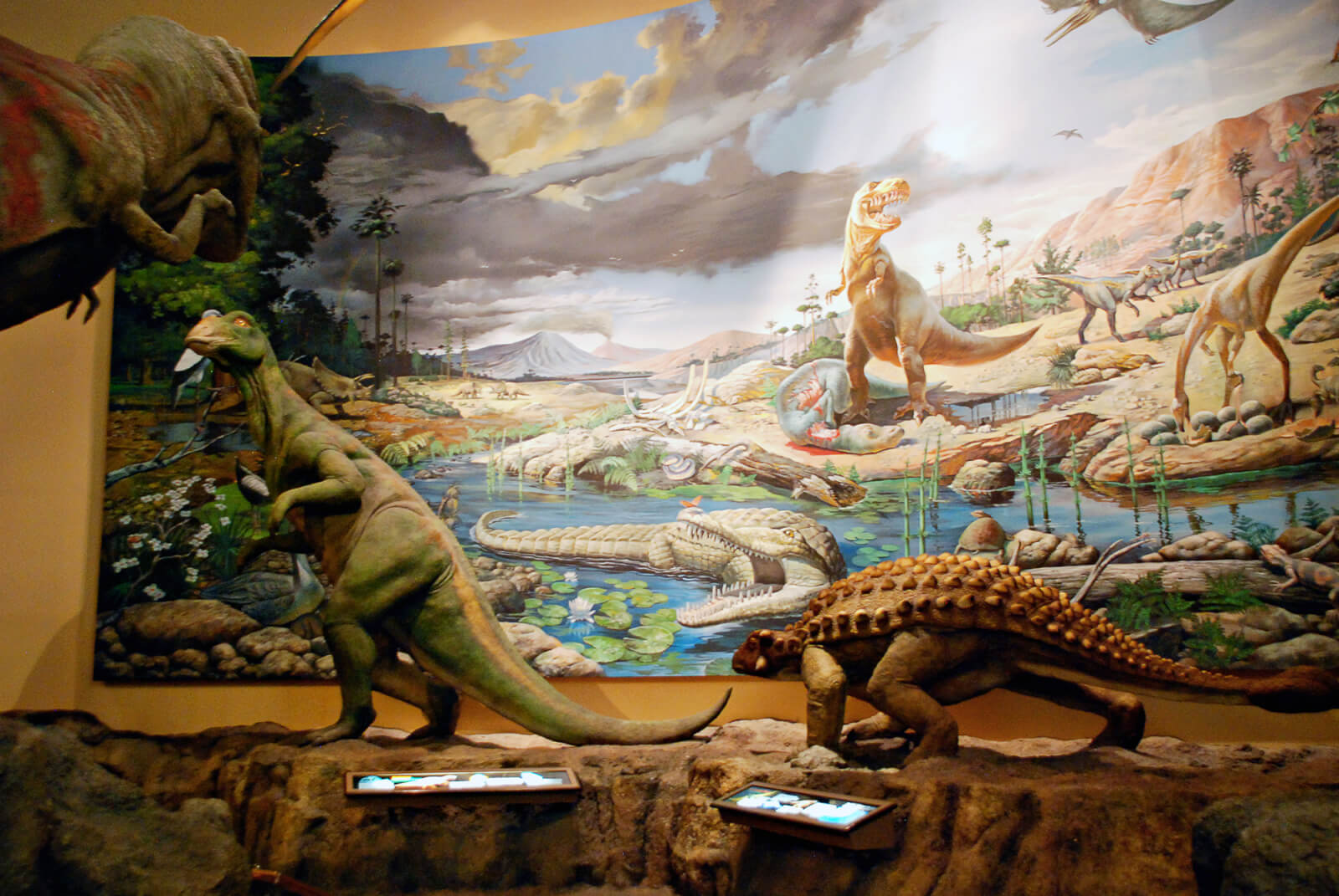 Three dinosaur statues stand in front of a painting of a scene in an exhibit at Fernbank Museum of Natural History in Atlanta Georgia. 